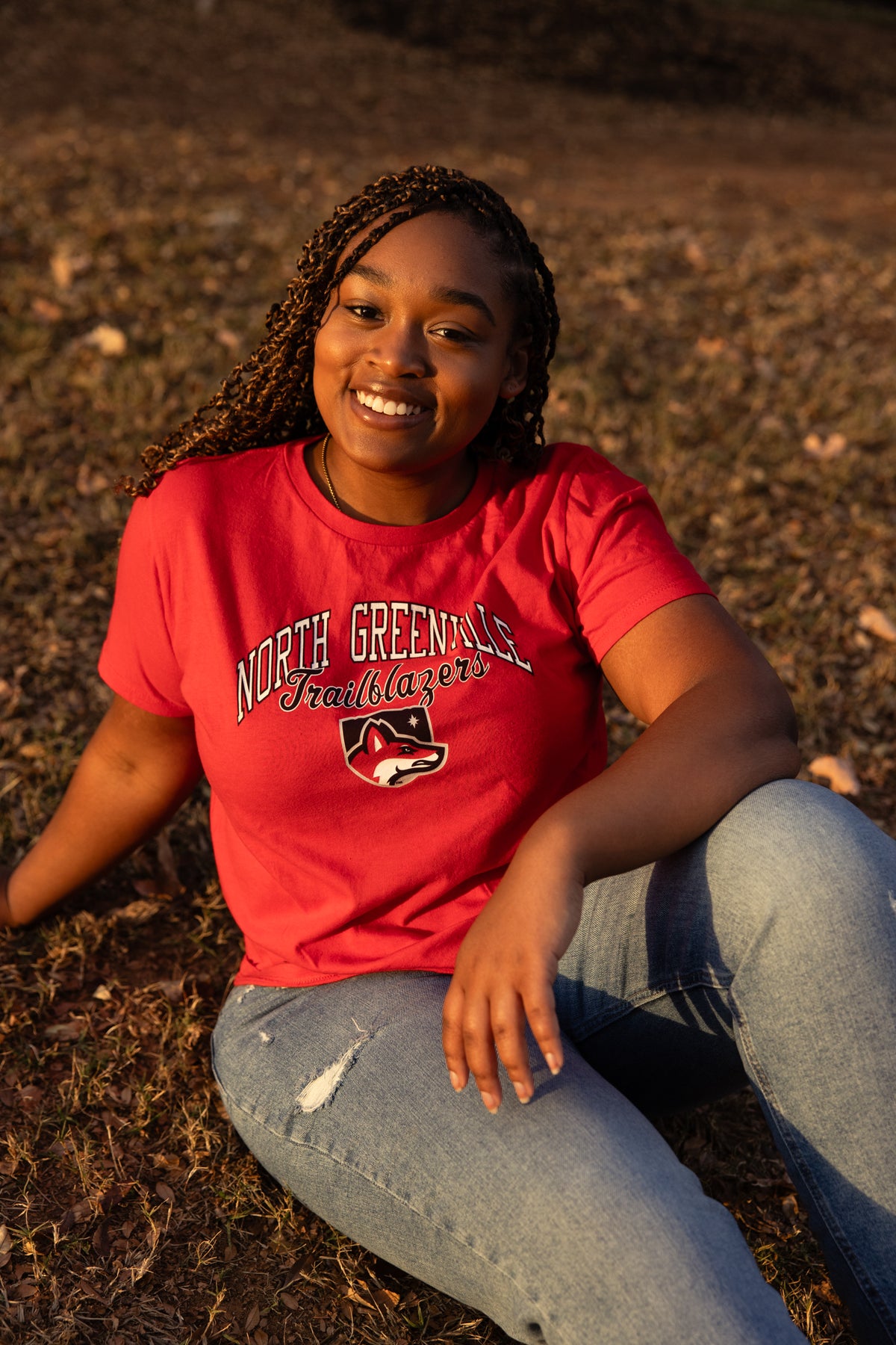 Woman wearing a red 'North Greenville' t-shirt sitting on the ground.
