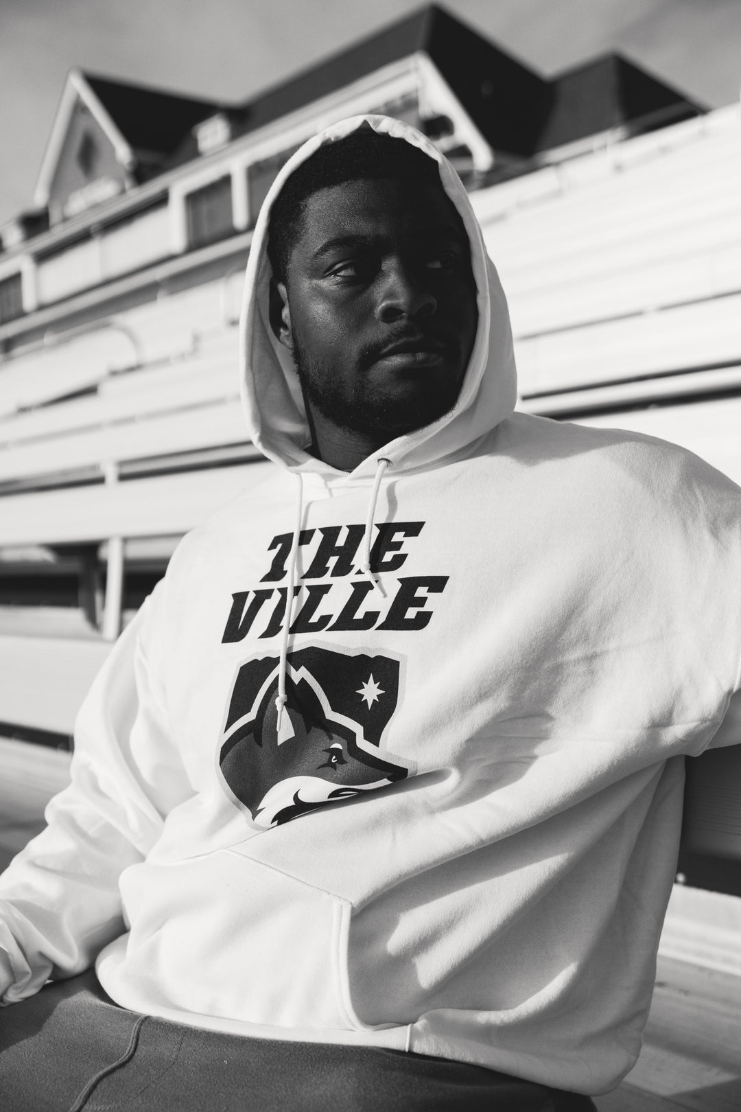 Man wearing a hoodie with 'The Ville' logo sitting outdoors.