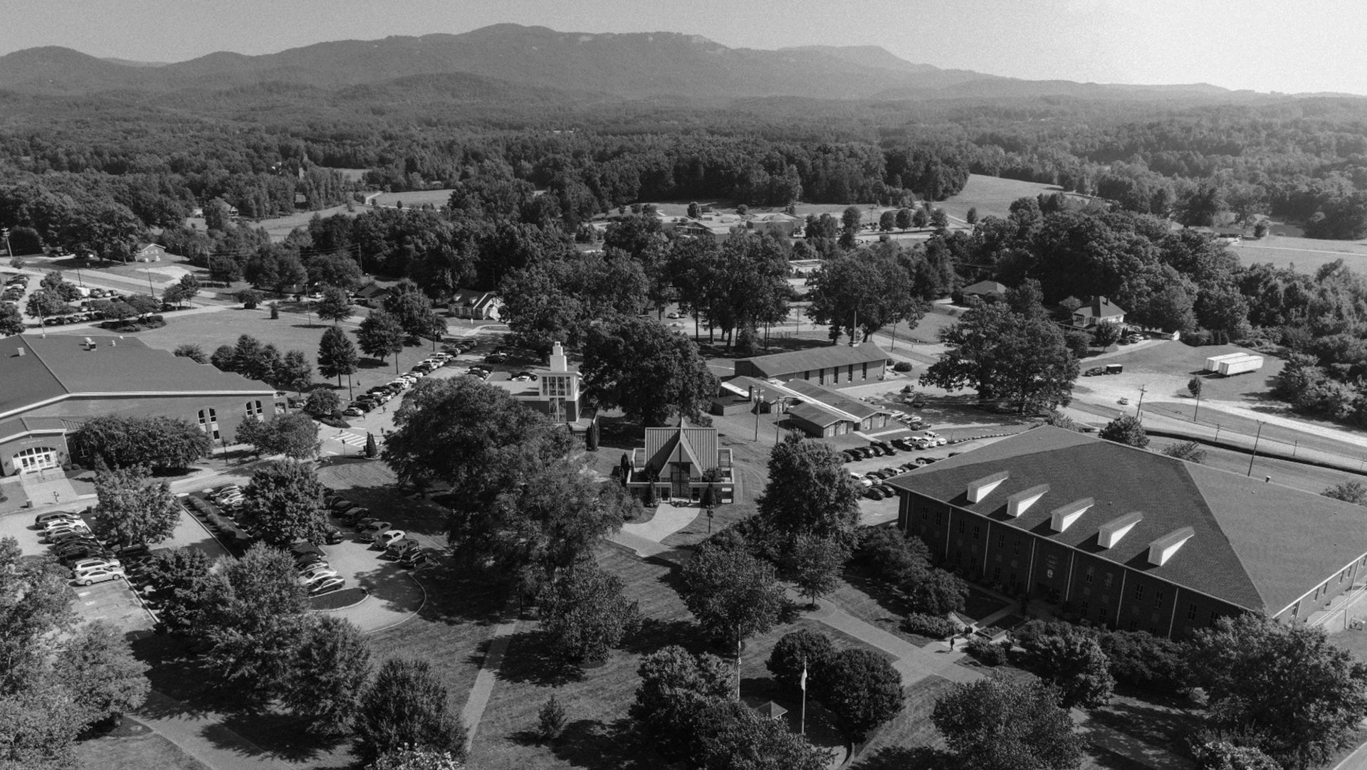 Aerial view of a campus with buildings and trees, surrounded by mountains.